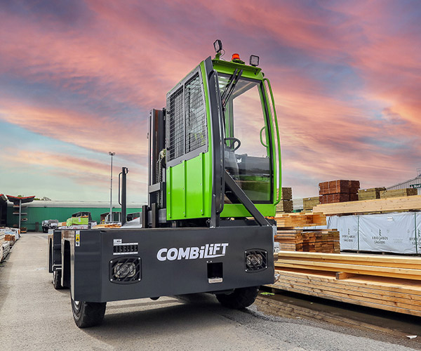 Combilift Seitenstapler (grün) mit Holzstapel bei Sonnenuntergang