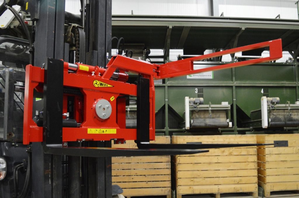 Rotes Anbaugeraet mit Schwenkarm vor Holzkisten