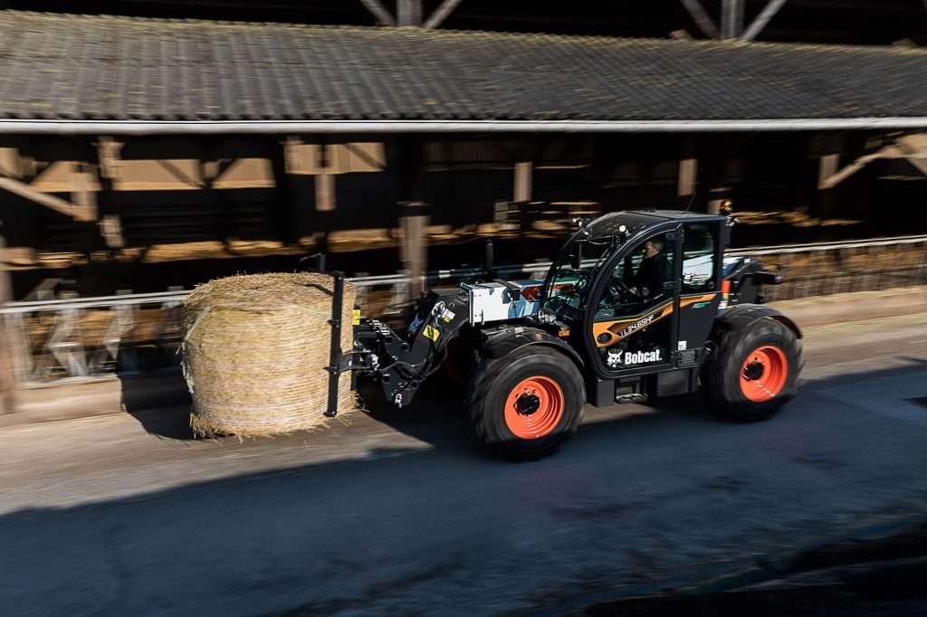 Bobcat Teleskoplader traegt Rundballen durch Stall