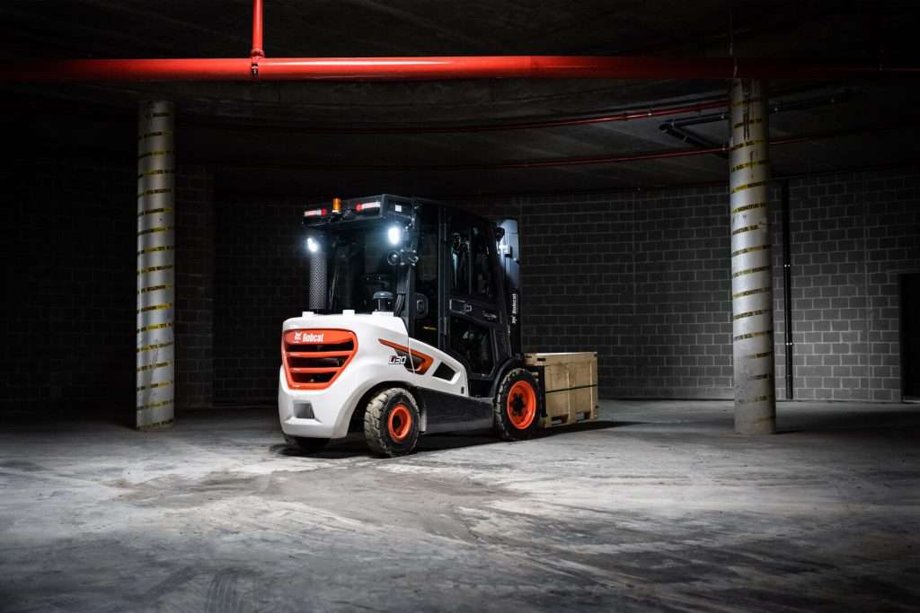 Bobcat Stapler mit Kabine in dunkler Betonhalle, rotes Licht