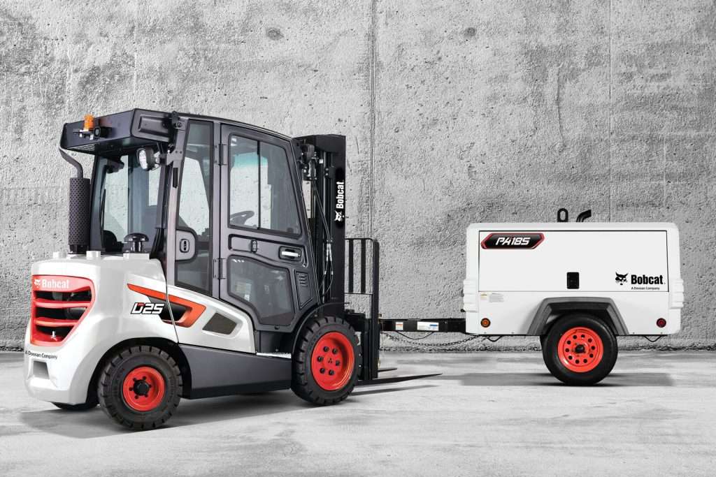 Bobcat Stapler mit Kabine vor Betonwand mit Kompressor