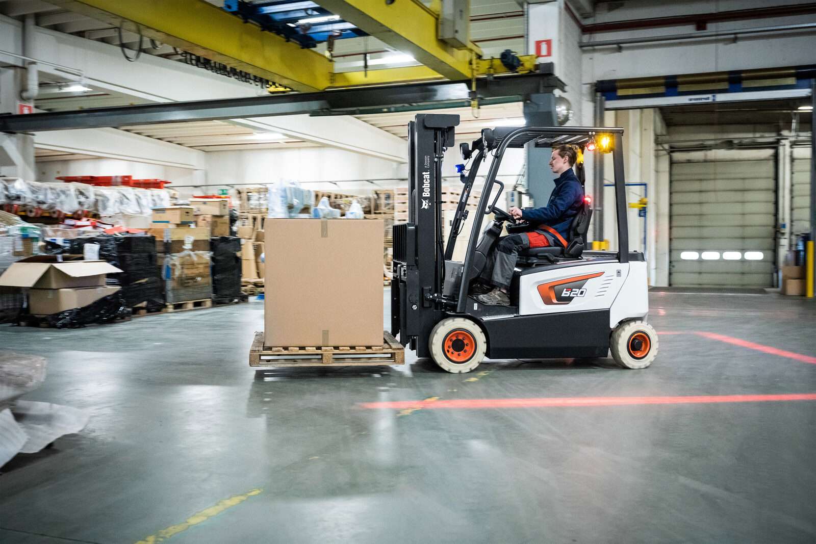 Bobcat Elektrostapler faehrt Karton durch Produktionshalle