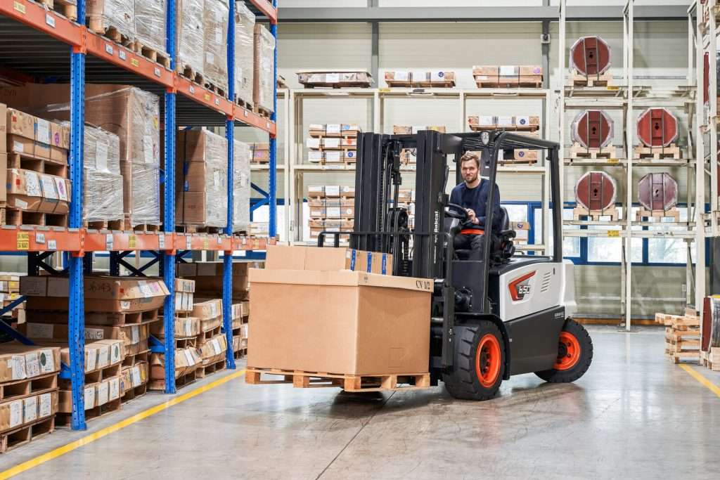 Bobcat Elektrostapler faehrt mit Kistenpalette durchs Lager