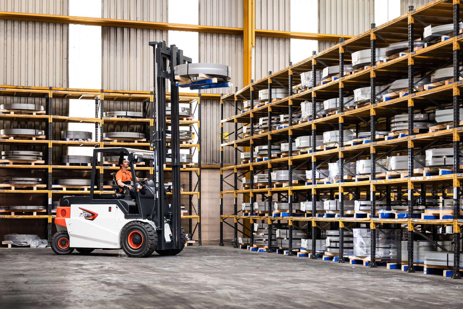Bobcat Stapler hebt Last ins hohe Regal einer Stahlhalle