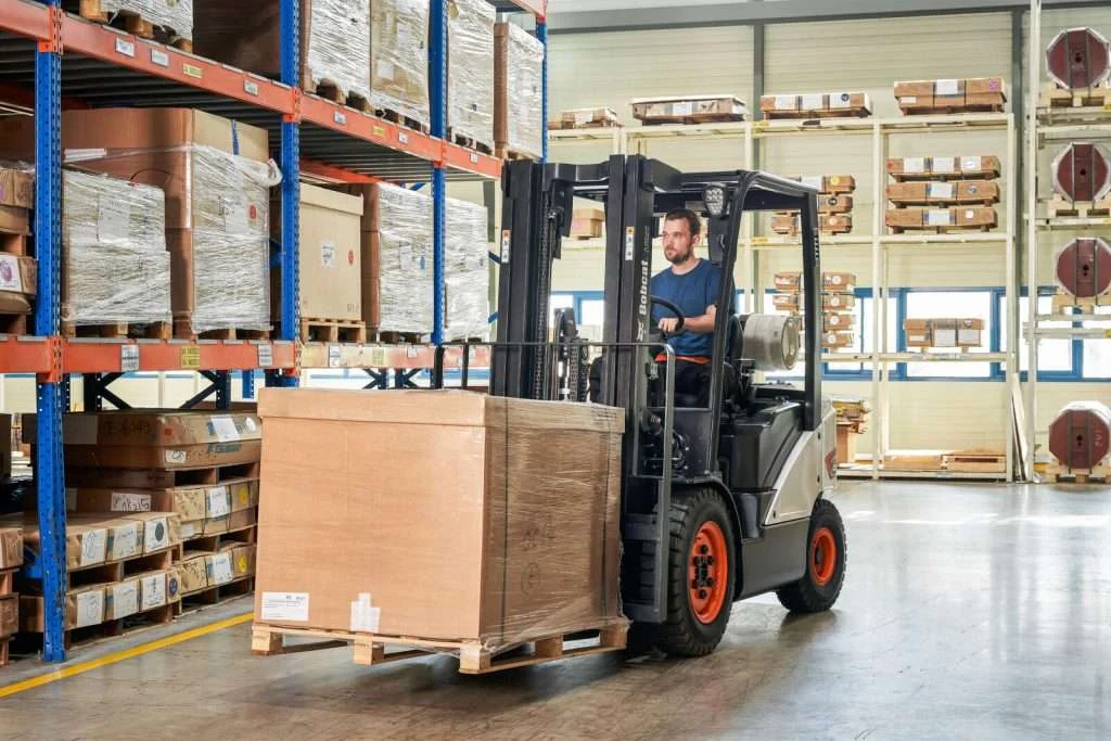 Bobcat Stapler mit Fahrer transportiert grossen Karton im Lager