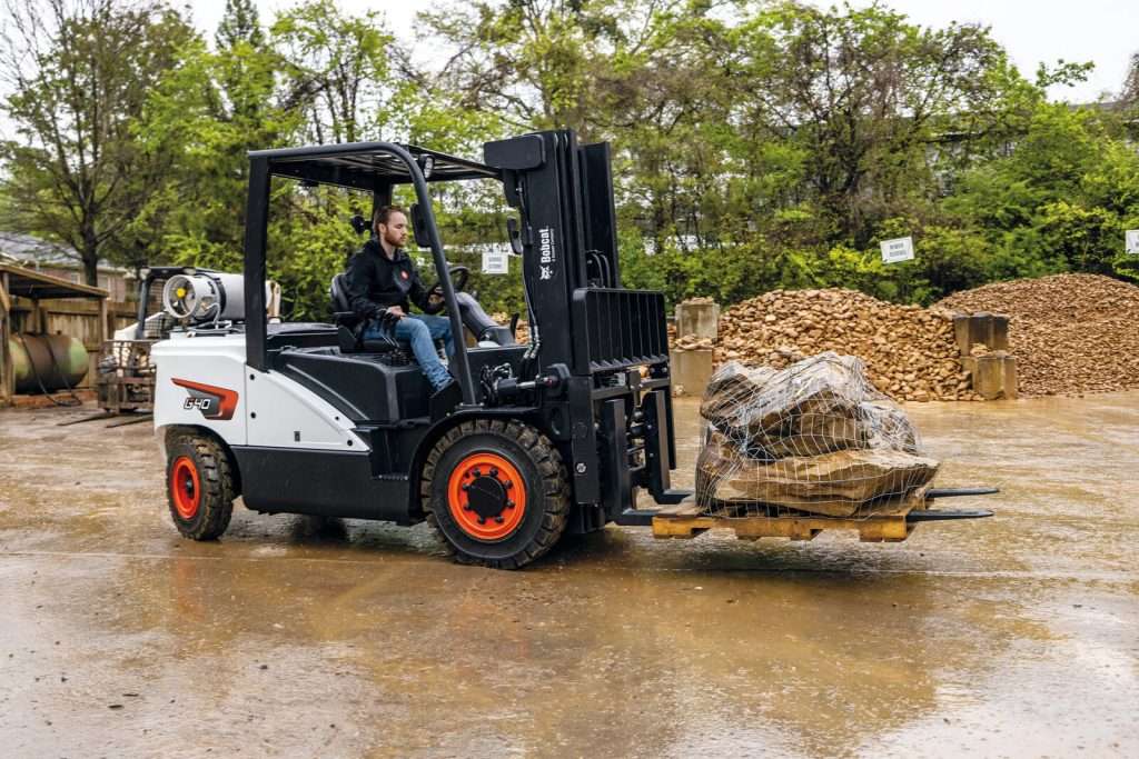 Bobcat Gasstapler mit Fahrer hebt Stein auf nassem Hof