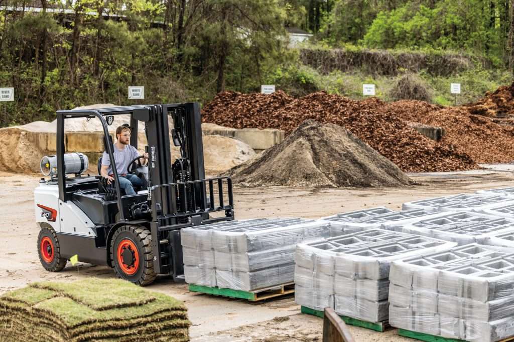 Bobcat Stapler mit Fahrer zwischen Rollrasen und Steinpaletten
