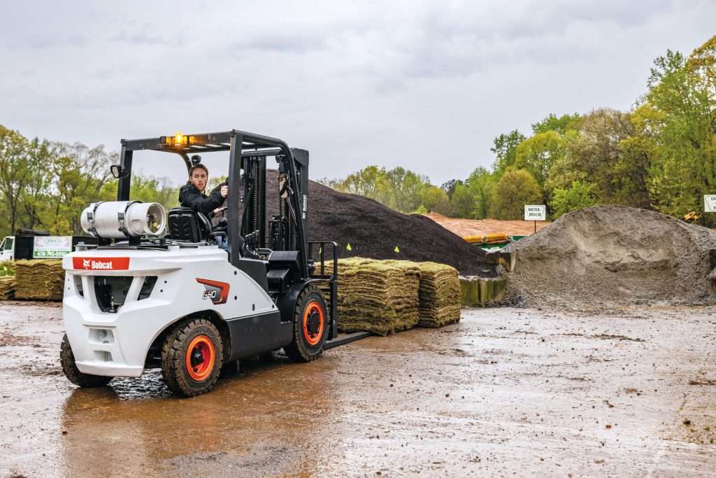Bobcat Stapler mit Fahrer vor Rollrasenpaletten auf Hof