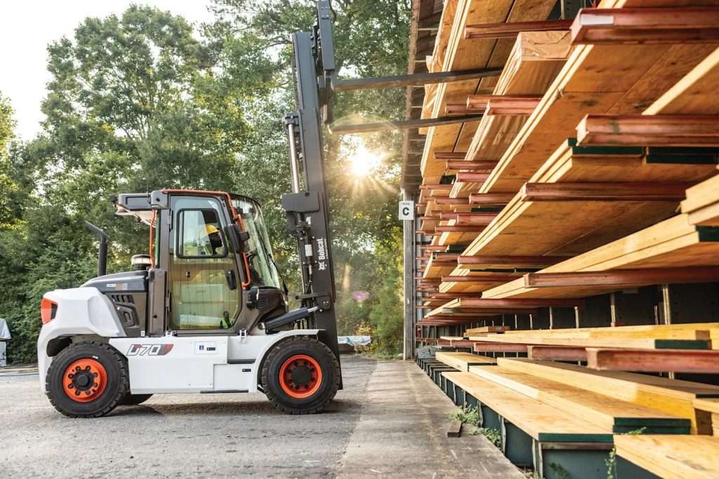 Bobcat D70S-9 von der Seite mit aufrechtem Mast neben einem Holzlager