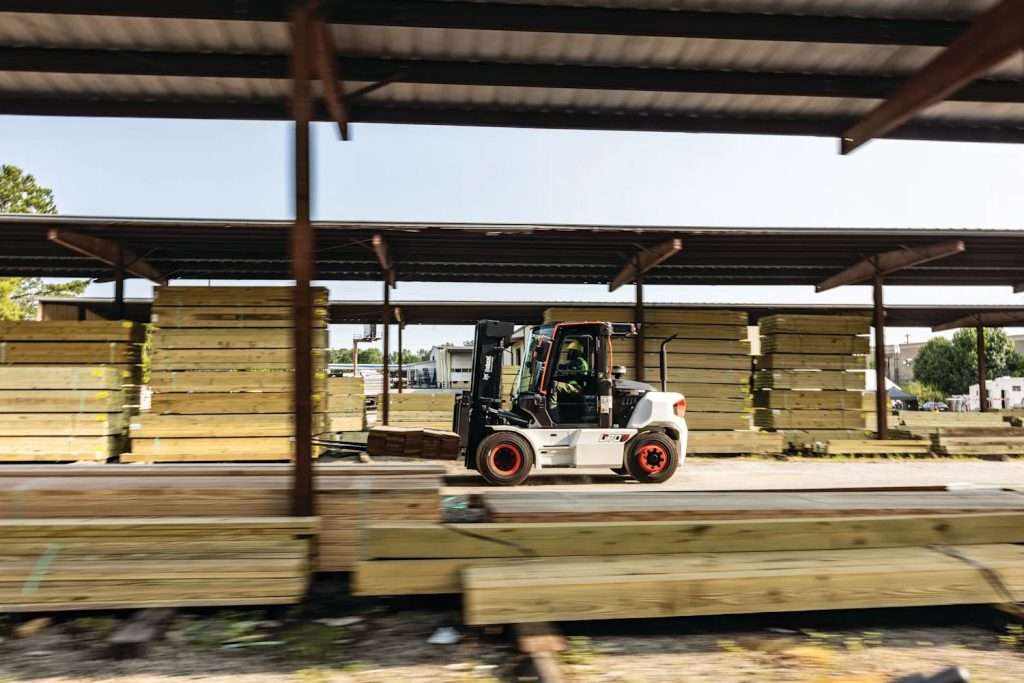 Bobcat D70S-9 fährt unter einem Hallendach an gestapeltem Schnittholz vorbei