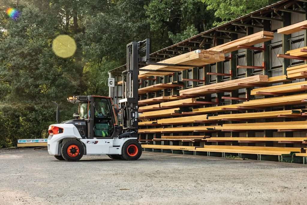 Bobcat D70S-9 fährt auf Schotter vor einem Kragarmregal mit Holz