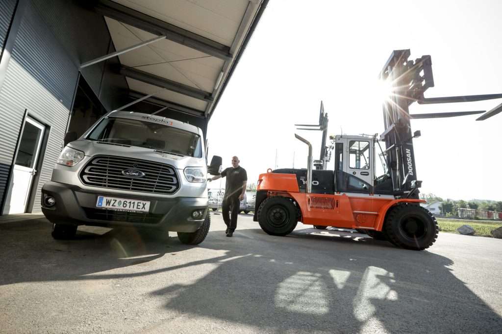 Oranger Doosan Stapler neben Transporter, Mitarbeiter dazwischen