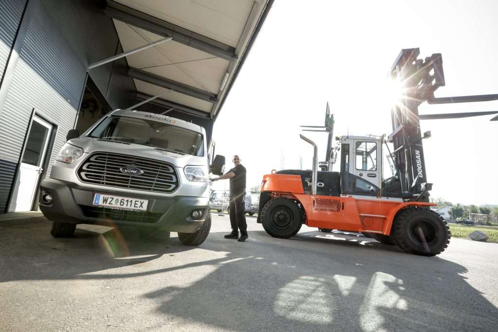 Oranger Doosan Stapler neben Transporter, Mitarbeiter dazwischen