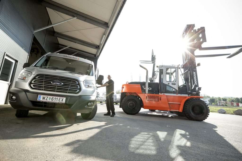 Oranger Doosan Stapler neben Transporter, Mitarbeiter dazwischen