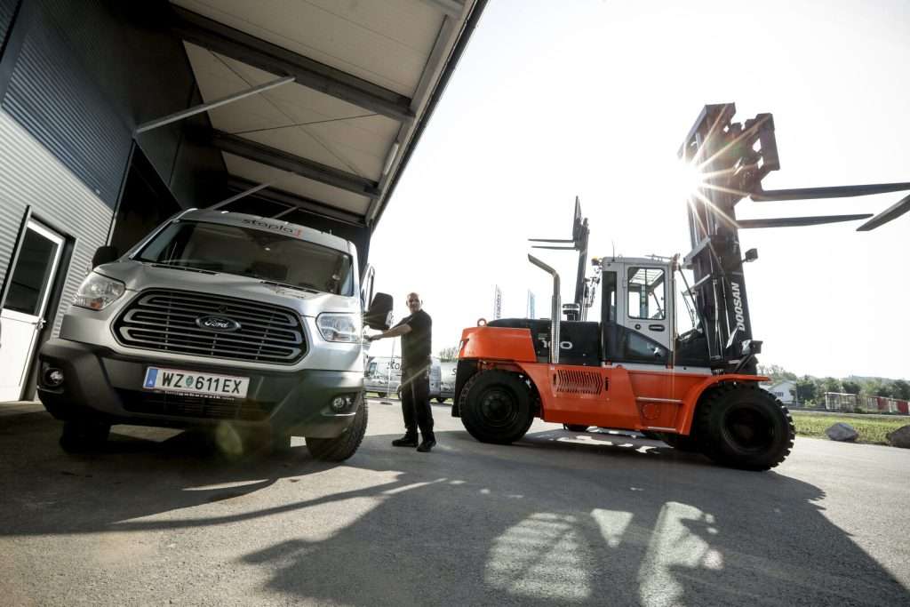 Oranger Doosan Stapler neben Transporter, Mitarbeiter dazwischen