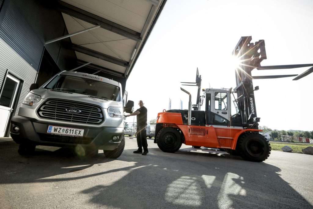 Oranger Doosan Stapler neben Transporter, Mitarbeiter dazwischen