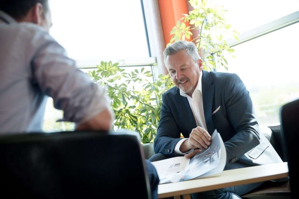Verkaufsberater zeigt Kunde Prospekt am Tisch