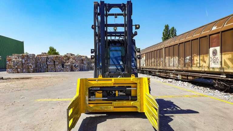 Gelbe Ballenklammer frontal am Stapler vor Papierballen und Waggon