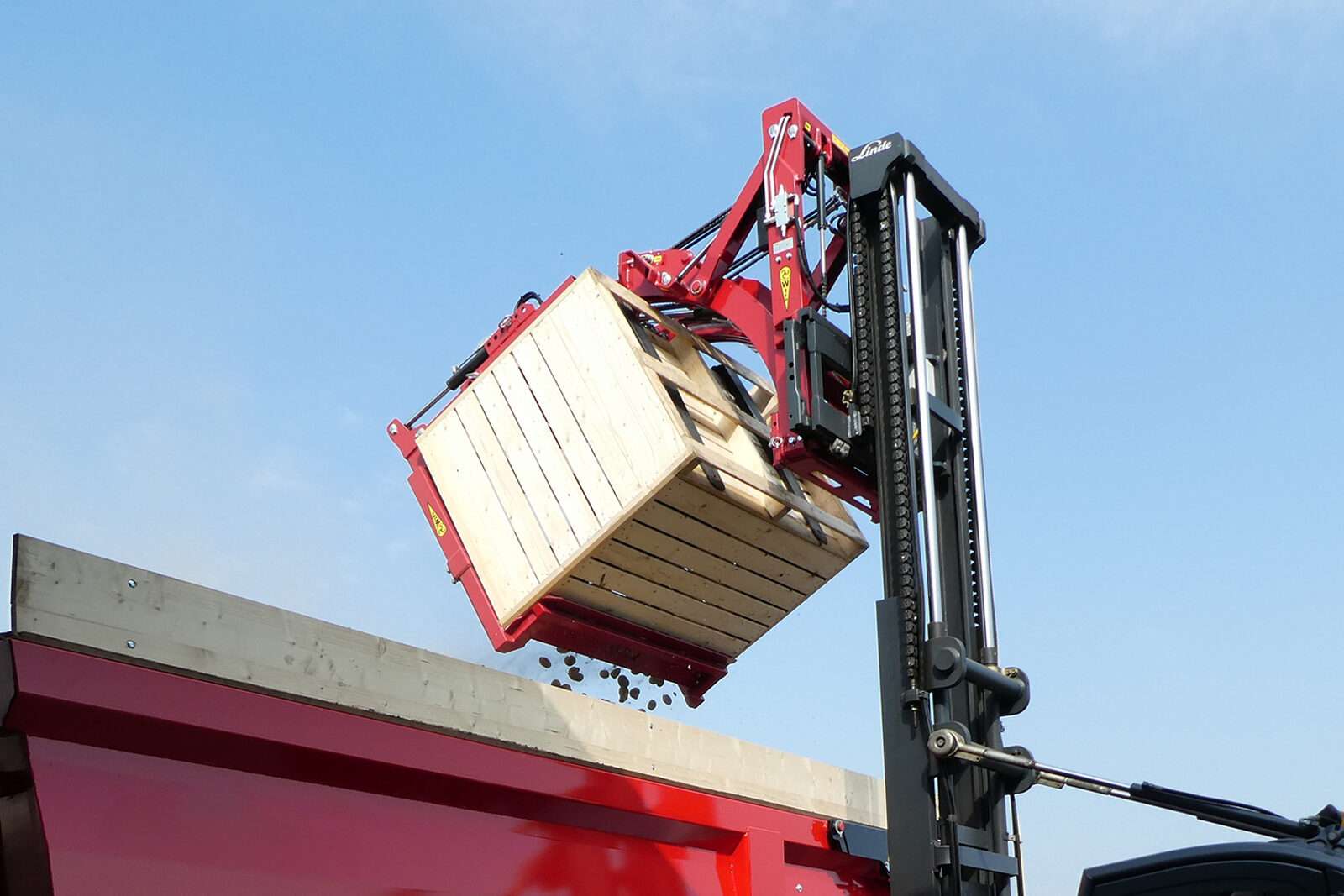 Stapler kippt Holzkiste mit WIFO-Kippgerät in roten Anhänger