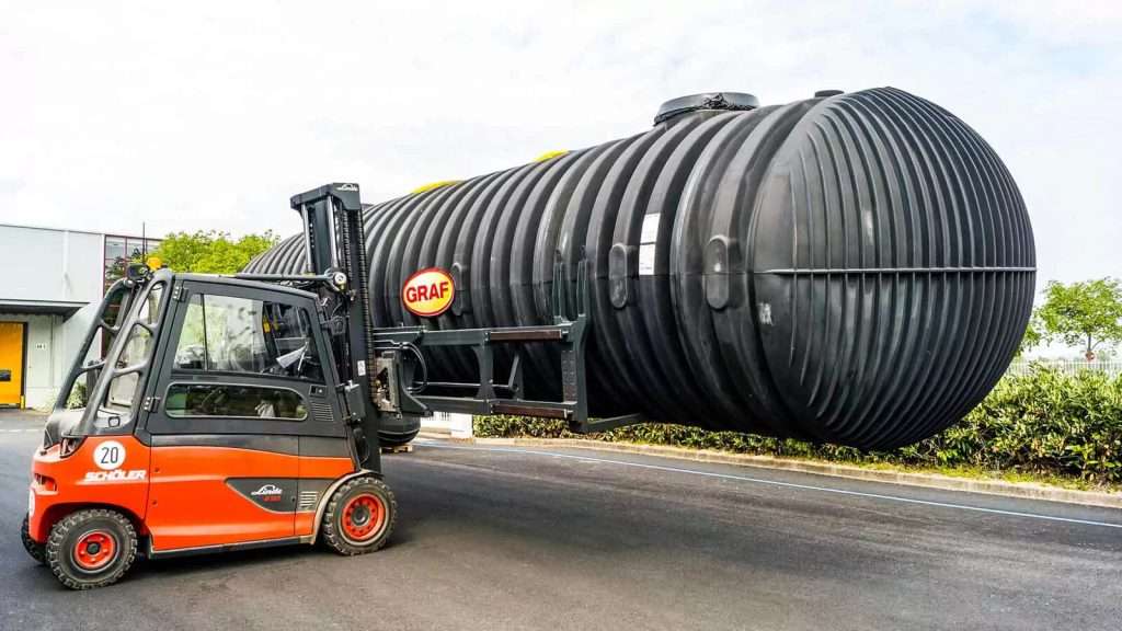 Stapler transportiert großen Tank mit gespreizten Gabeln
